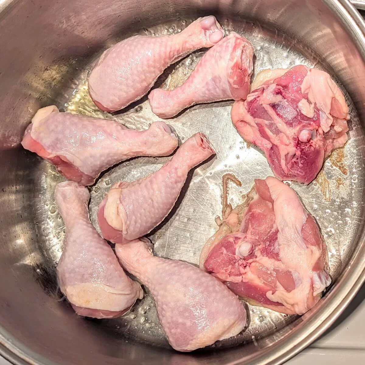 Chicken pieces in a heavy-bottomed pot being seared for preserved lemon chicken thighs