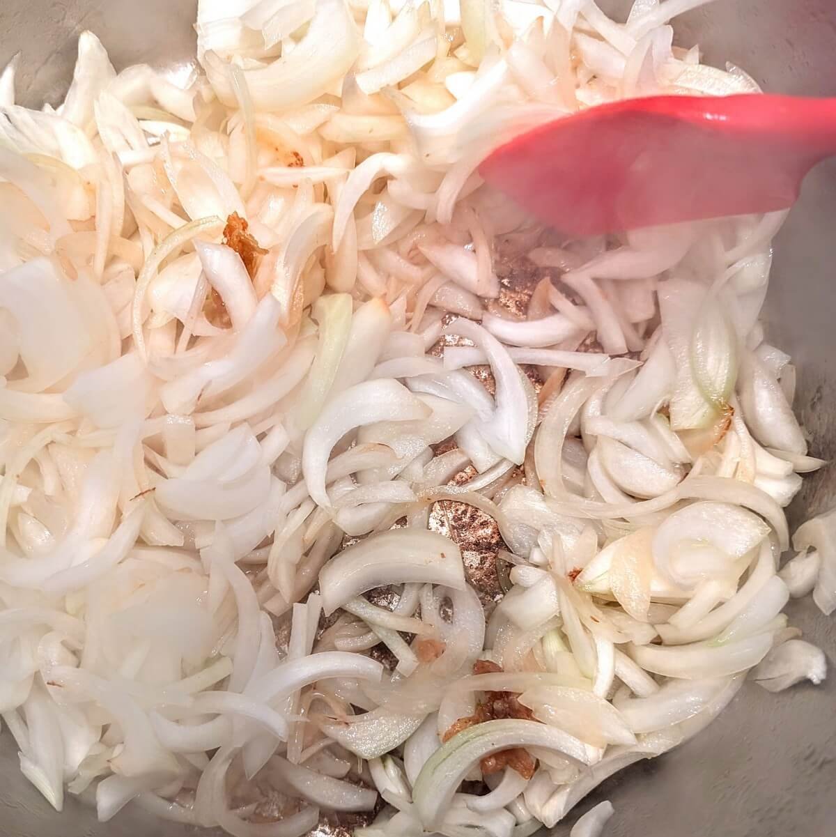 Sliced onions stirred in a pot with chicken fond to start a stovetop chicken tagine