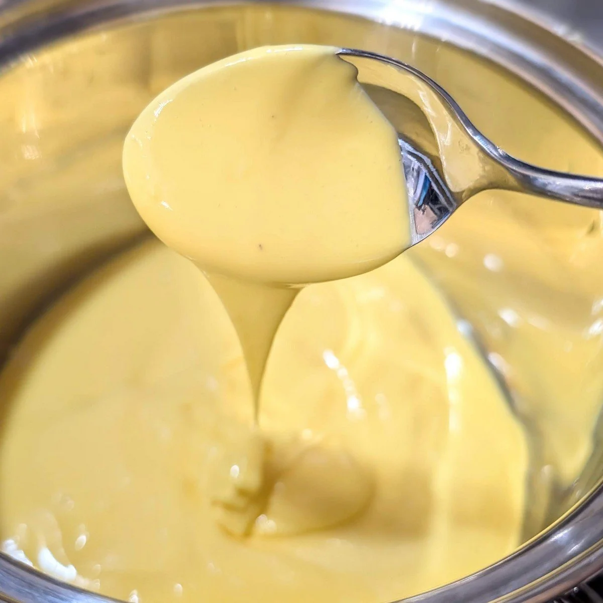 Foolproof immersion blender hollandaise in a saucepan with spoon drizzle sauce