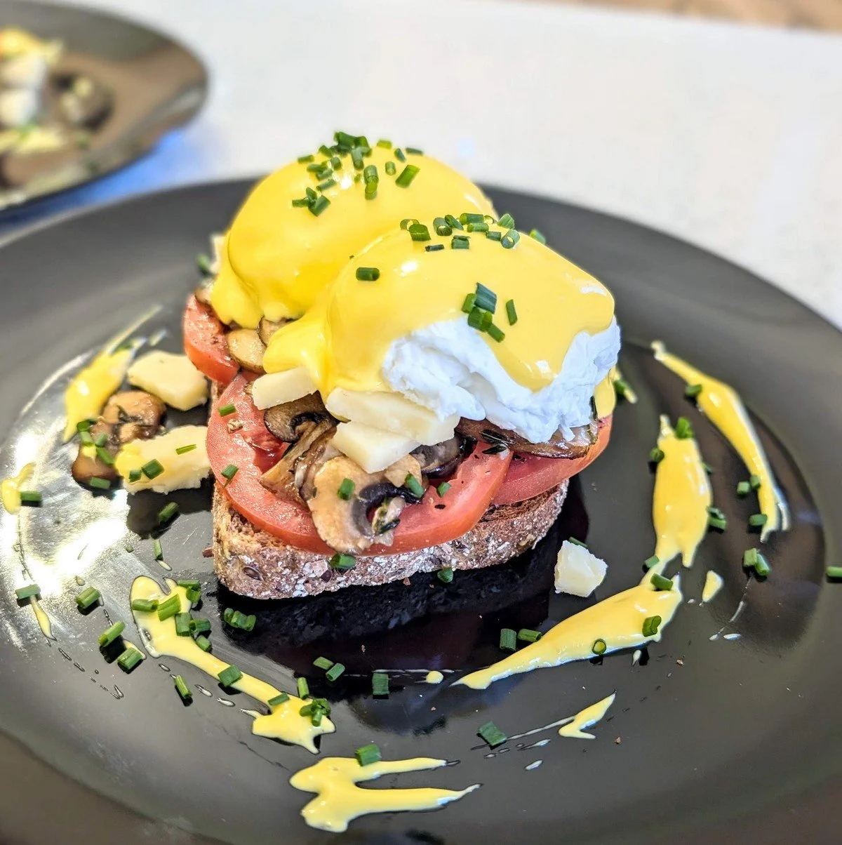 Homemade stick blender hollandaise on eggs benedict on a black plate