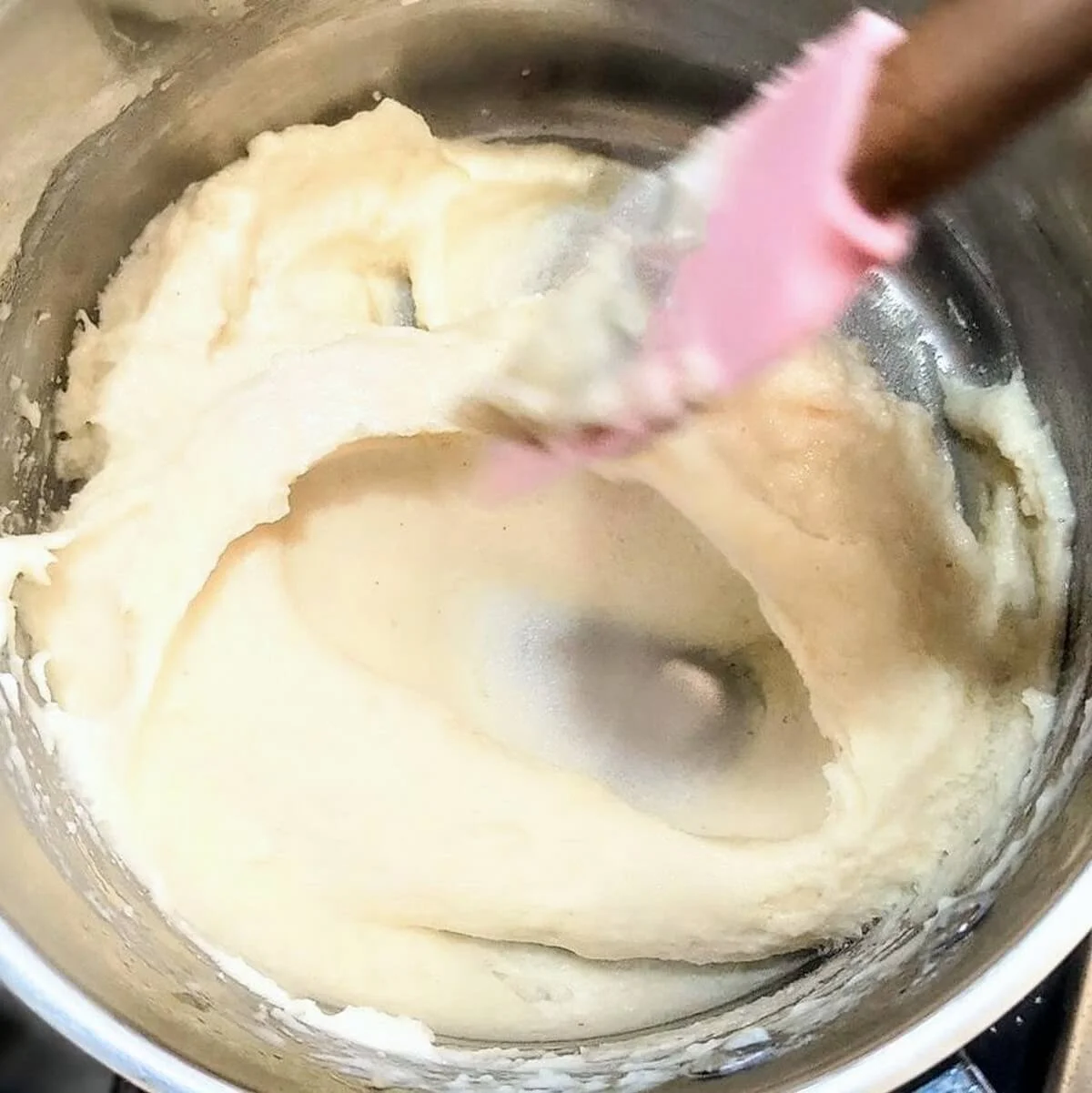 Bechamel sauce thickening and being stirred with a spatula in a saucepan