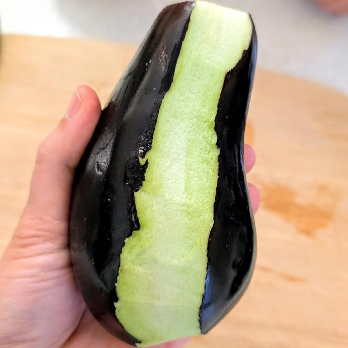 Eggplant with one strip of skin peeled off before slicing for Iraqi eggplant stew