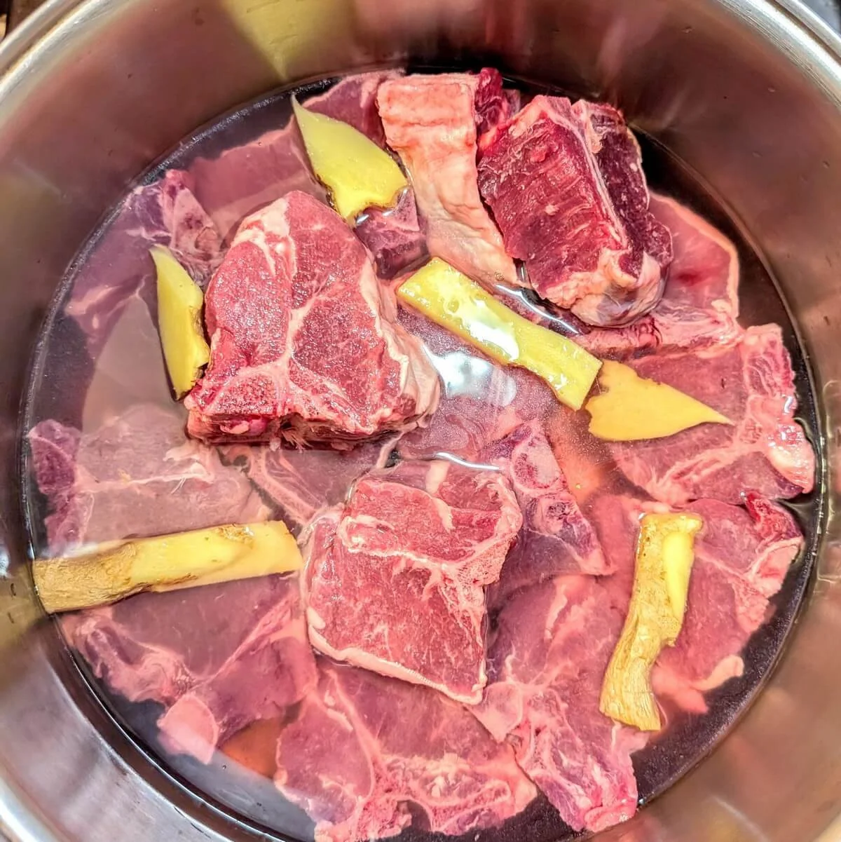 Lamb partially covered with water and sliced ginger before simmering