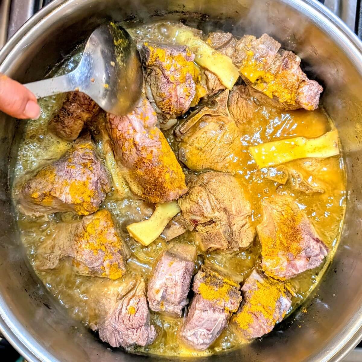 Turmeric and curry powder being stirred into a pot of simmering lamb for Iraqi lamb and eggplant stew