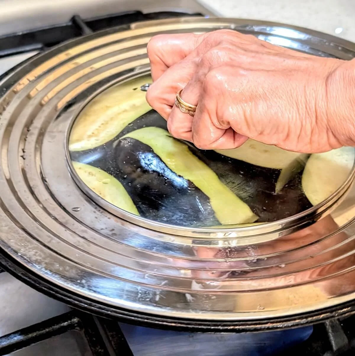 Lid being placed over eggplant while it sears in a non-stick pan