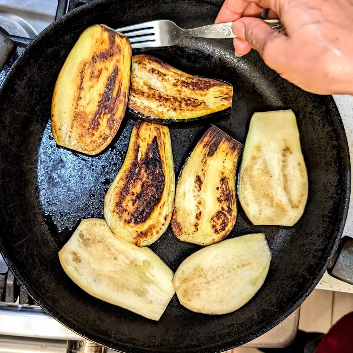 Eggplant being flipped with a fork to check browning on one side