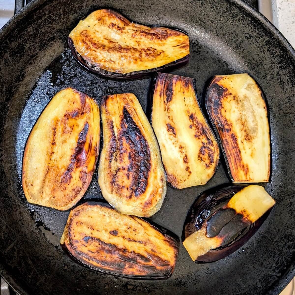 Eggplant slices deeply browned in a skillet during cooking