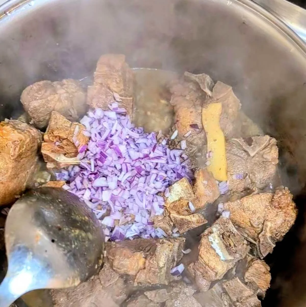 Chopped onions being added to braised lamb in the pot