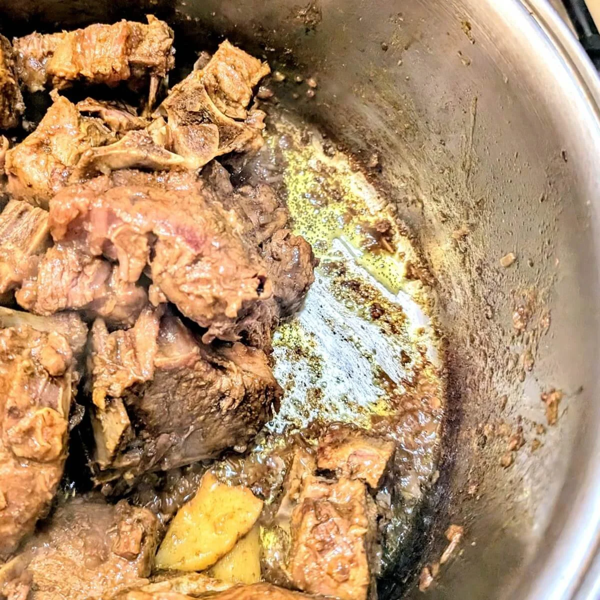 Lamb chops in a pot with the liquid fully reduced and oil visible at the bottom