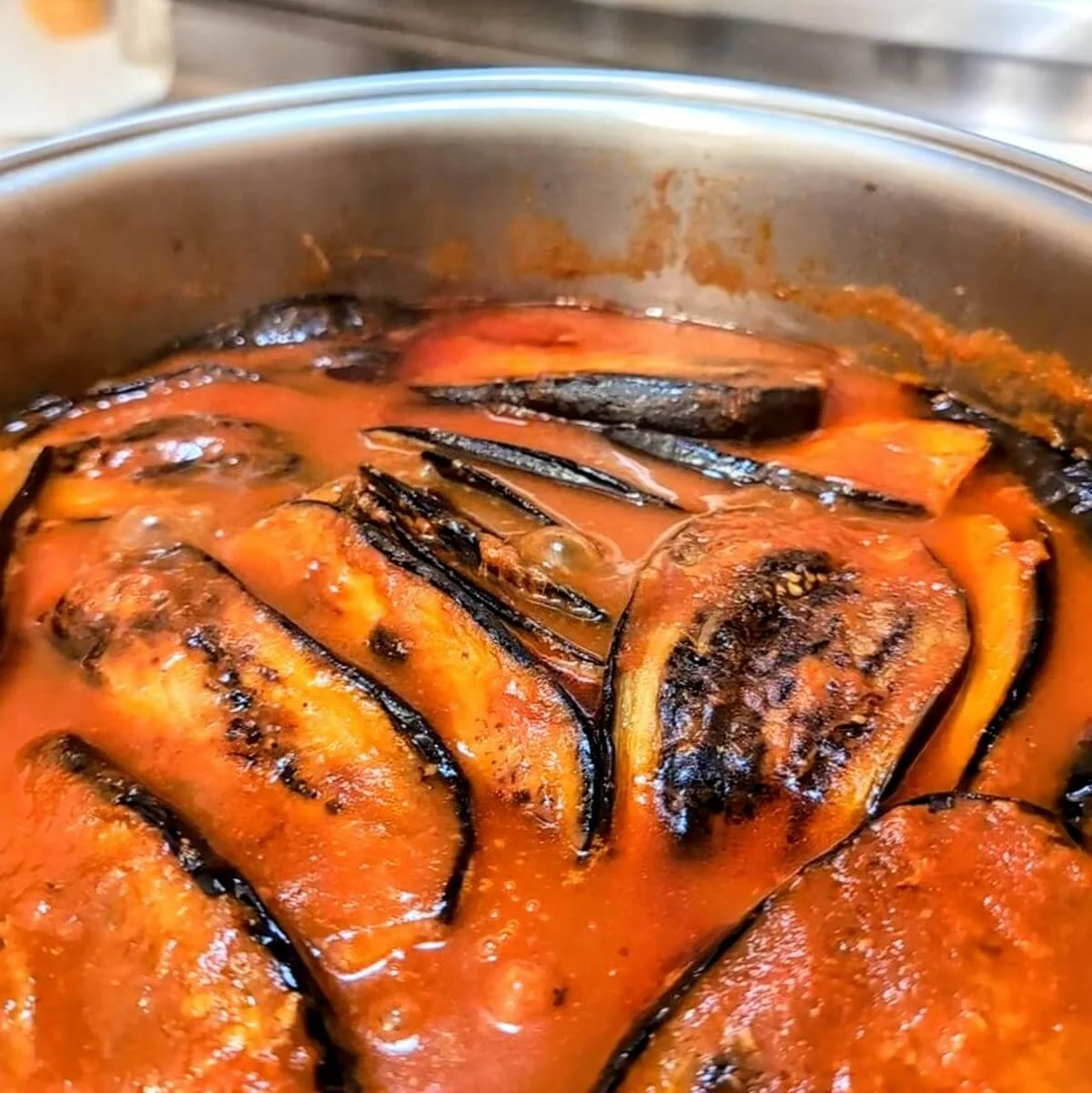 Close-up of eggplant layered over lamb stew with tomato sauce gently bubbling