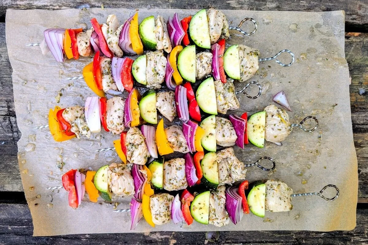 Assembled chicken and veggie skewers for camping arranged on parchment paper on a picnic table