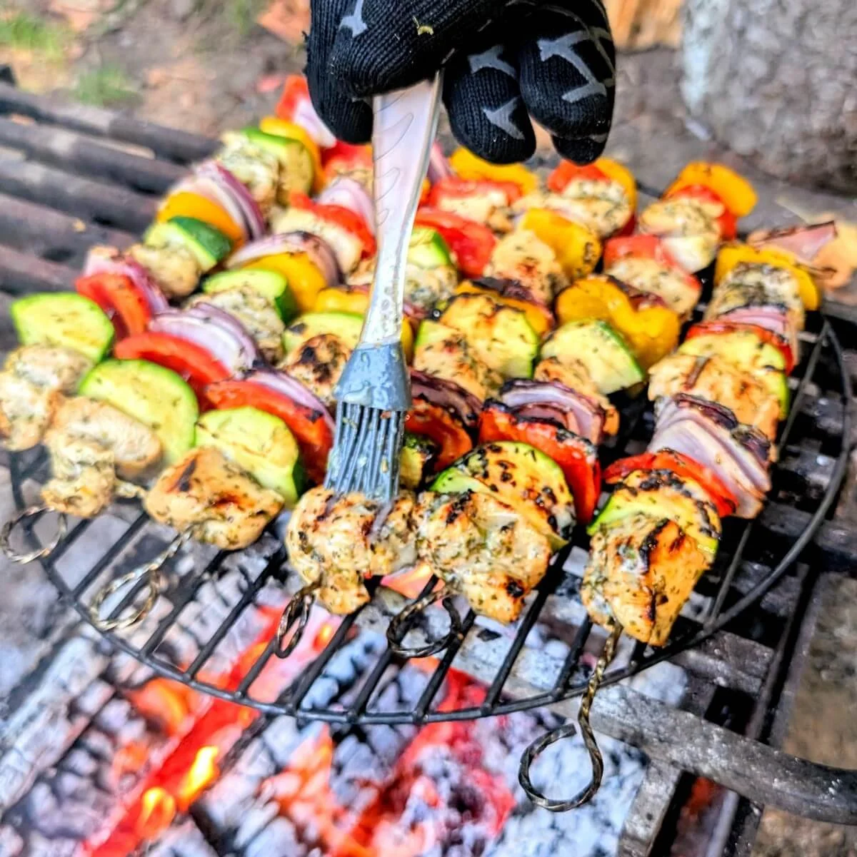 Hand brushing marinade onto campfire grilled chicken skewers