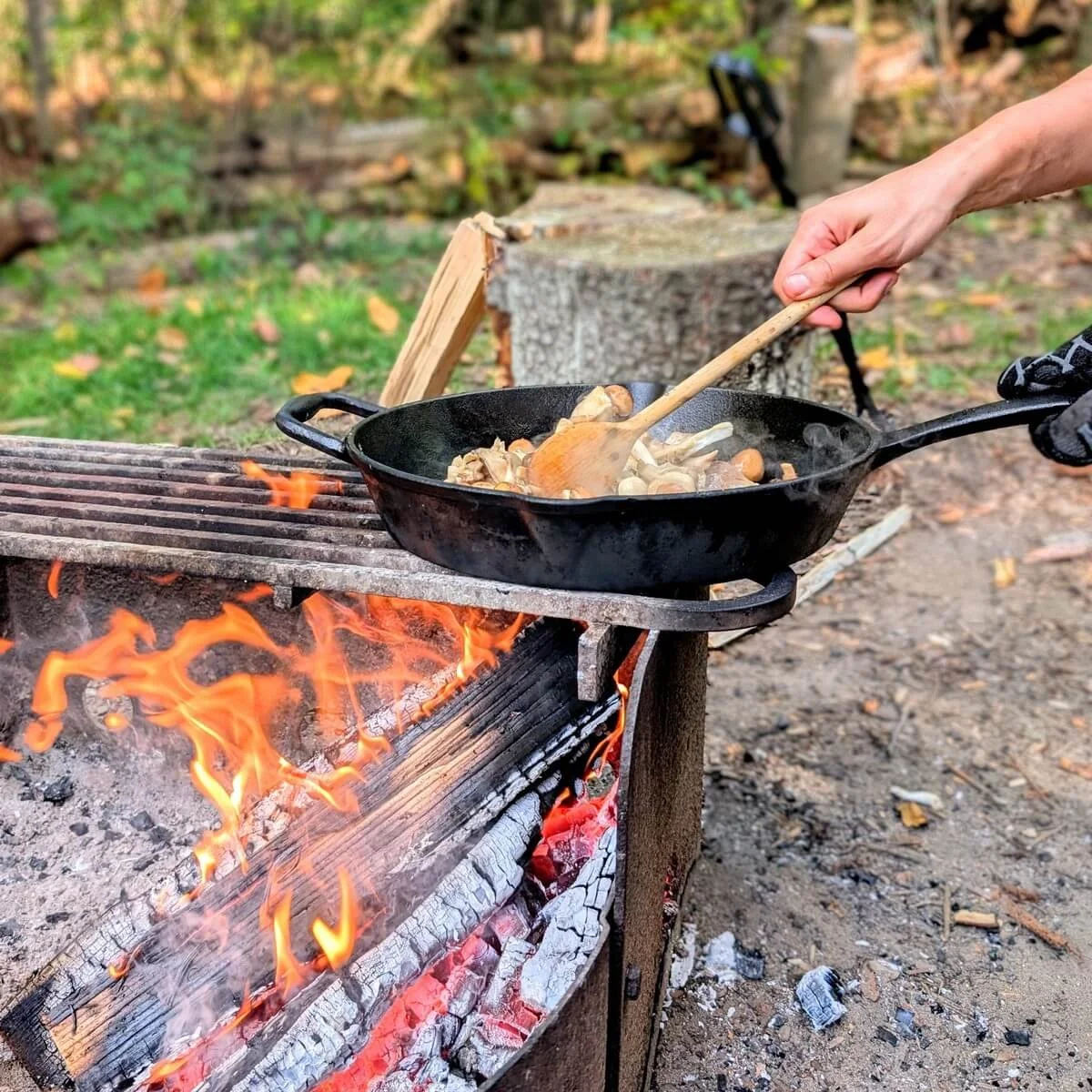 Stirring mixed mushrooms in cast iron pan over fire for camping risotto