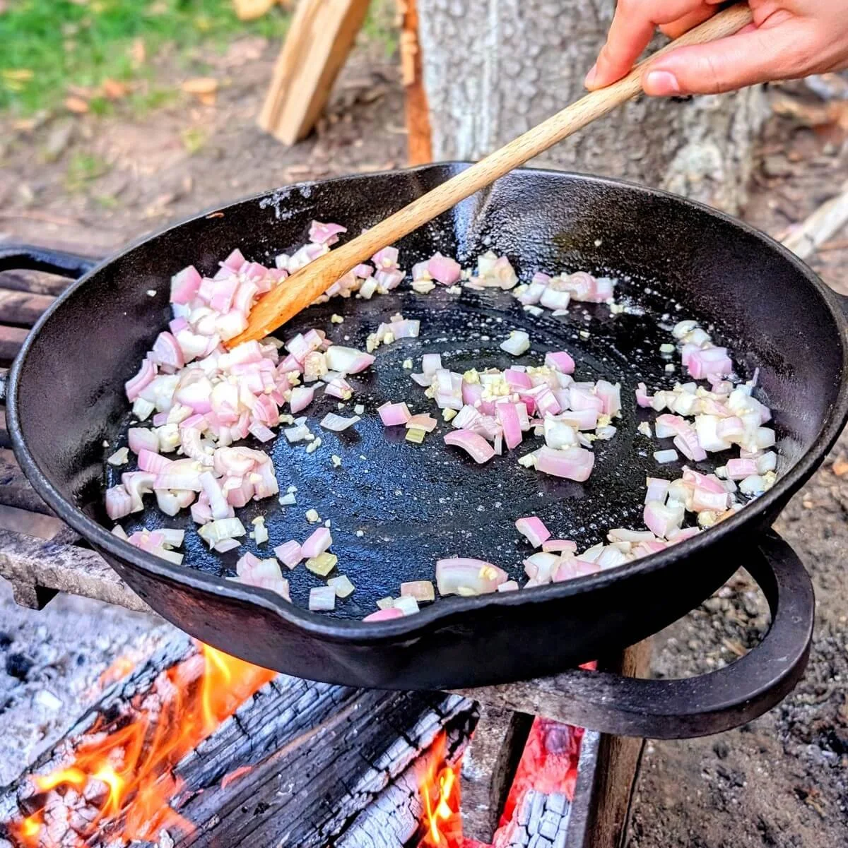 Campfire risotto with shallots and garlic cooking in a cast iron pan over an open fire