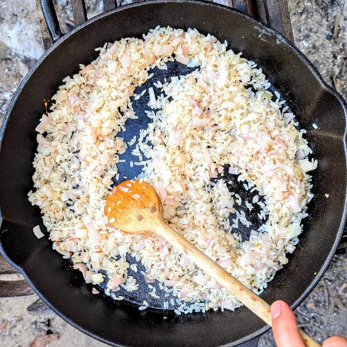 Toasting arborio rice with shallots in a cast iron pan for campfire mushroom risotto