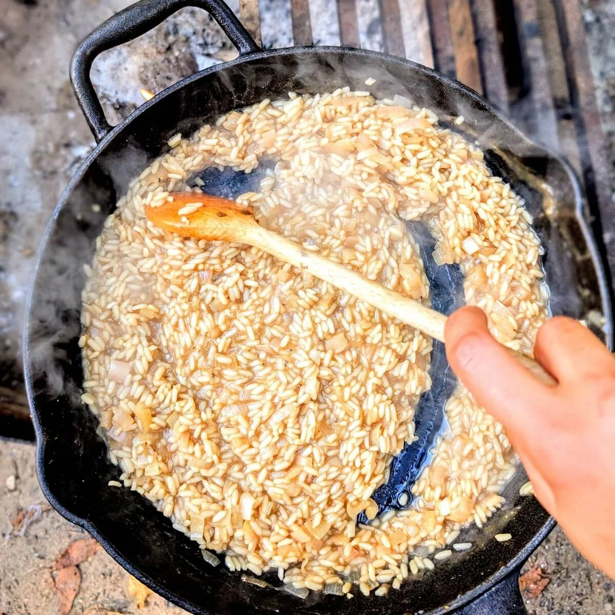 Overhead view of arborio rice simmering in mushroom broth until creamy and al dente in cast iron skillet