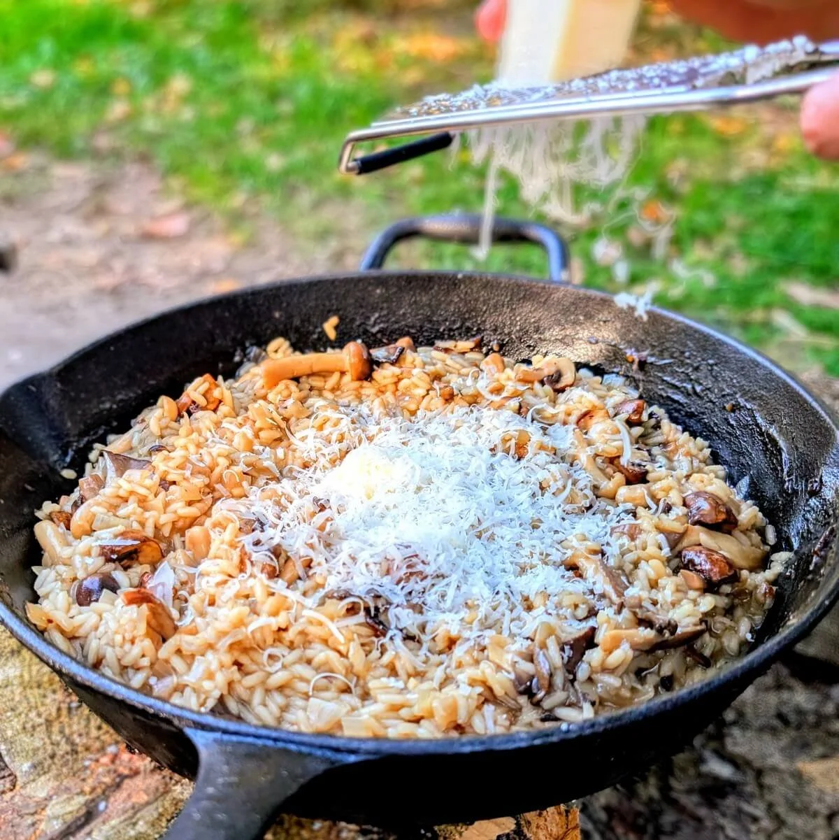 Grating hard cheese over hot risotto in cast iron pan for camping risotto