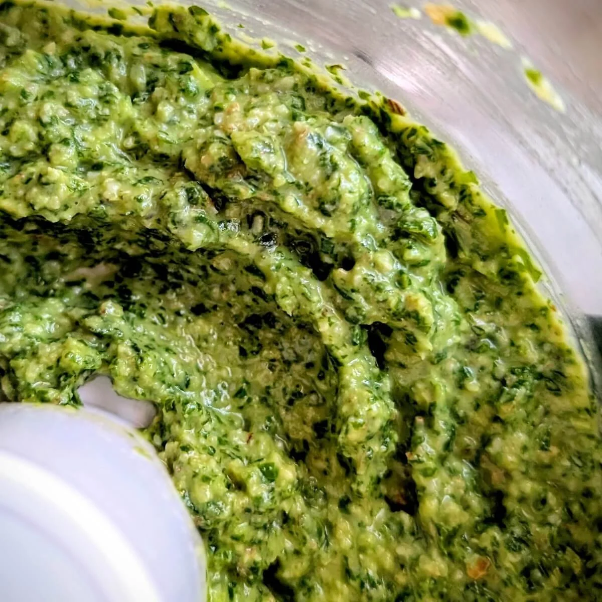 Closeup of smooth arugula basil walnut pesto in the bowl of a food processor