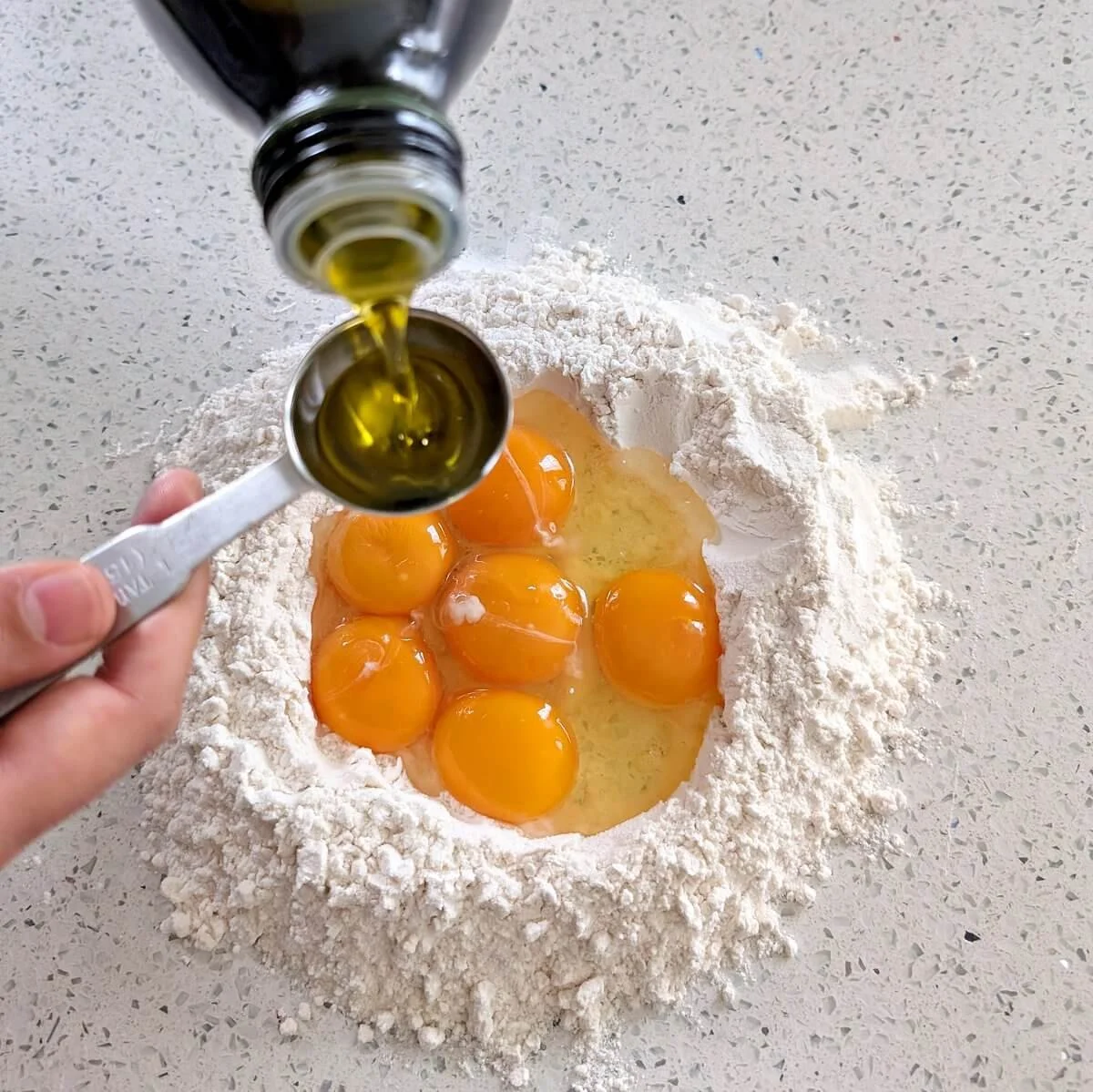 Olive oil being poured into egg-filled flour well for fresh egg pasta dough