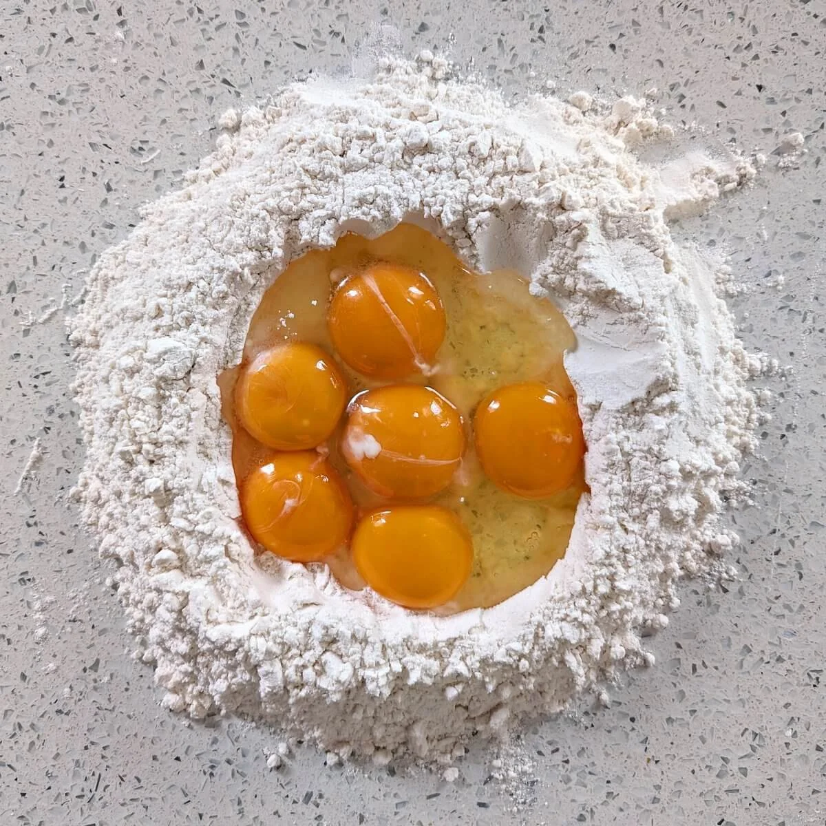 Flour well on a countertop filled with whole eggs and yolks before mixing pasta dough