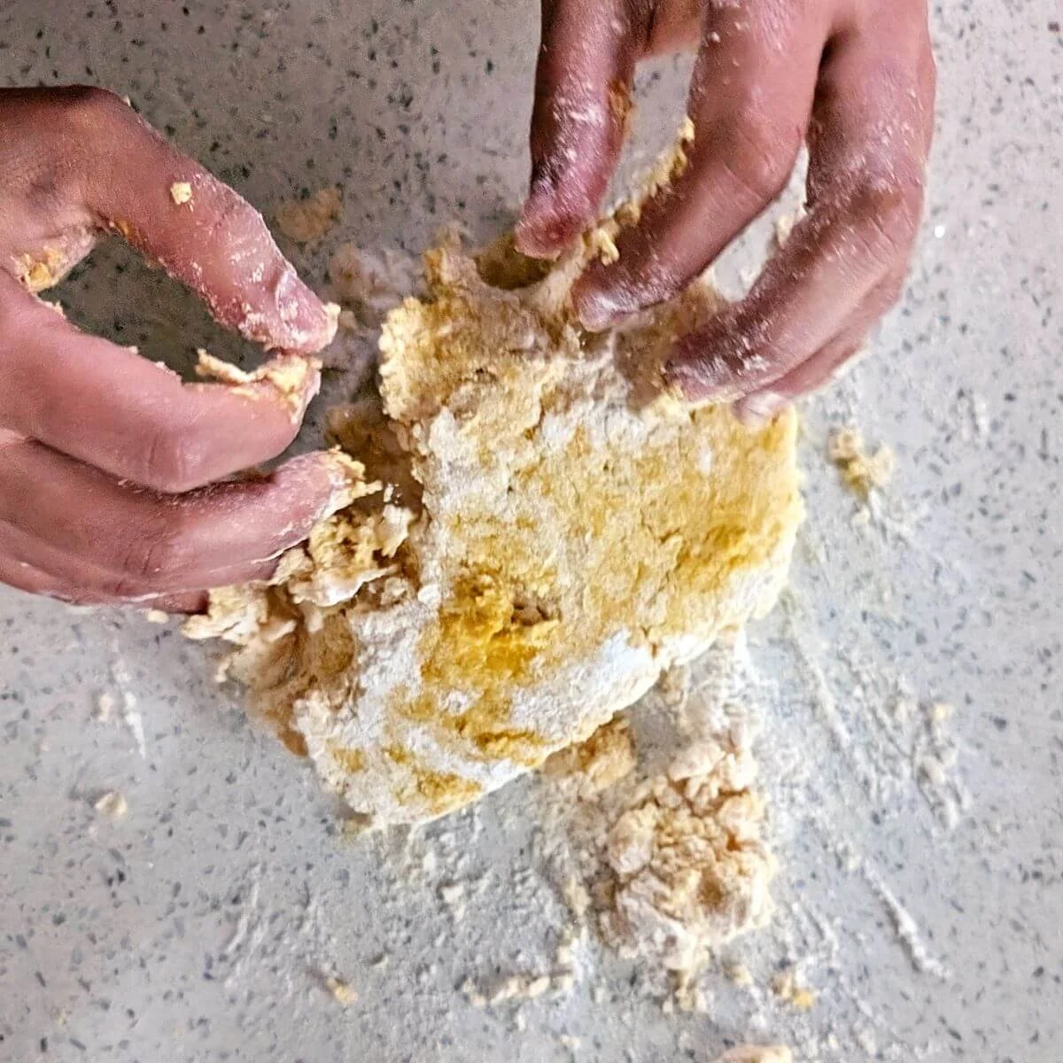 Hands pressing and folding shaggy egg pasta dough together on the counter