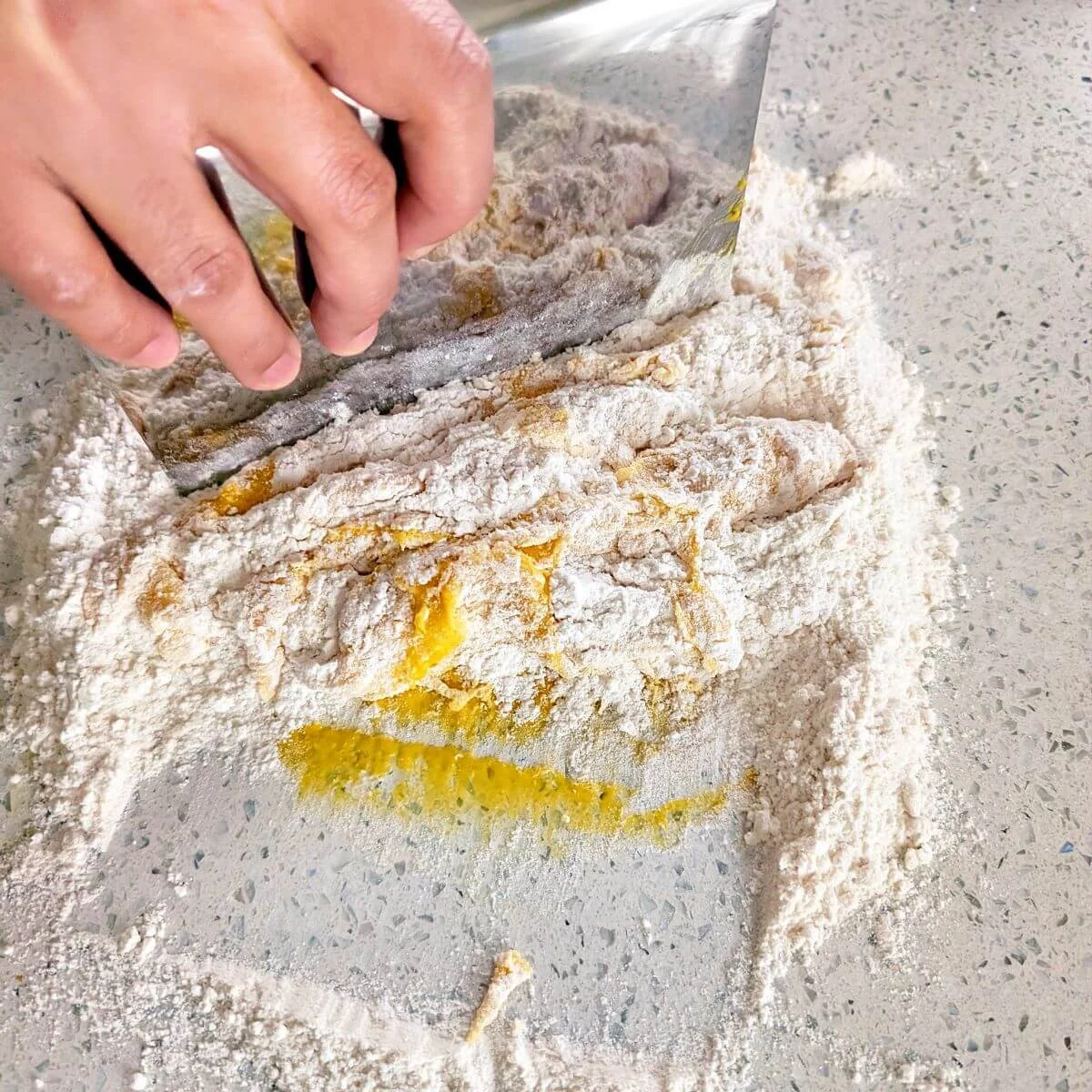 Bench scraper cutting flour into the wet center to help combine the pasta dough