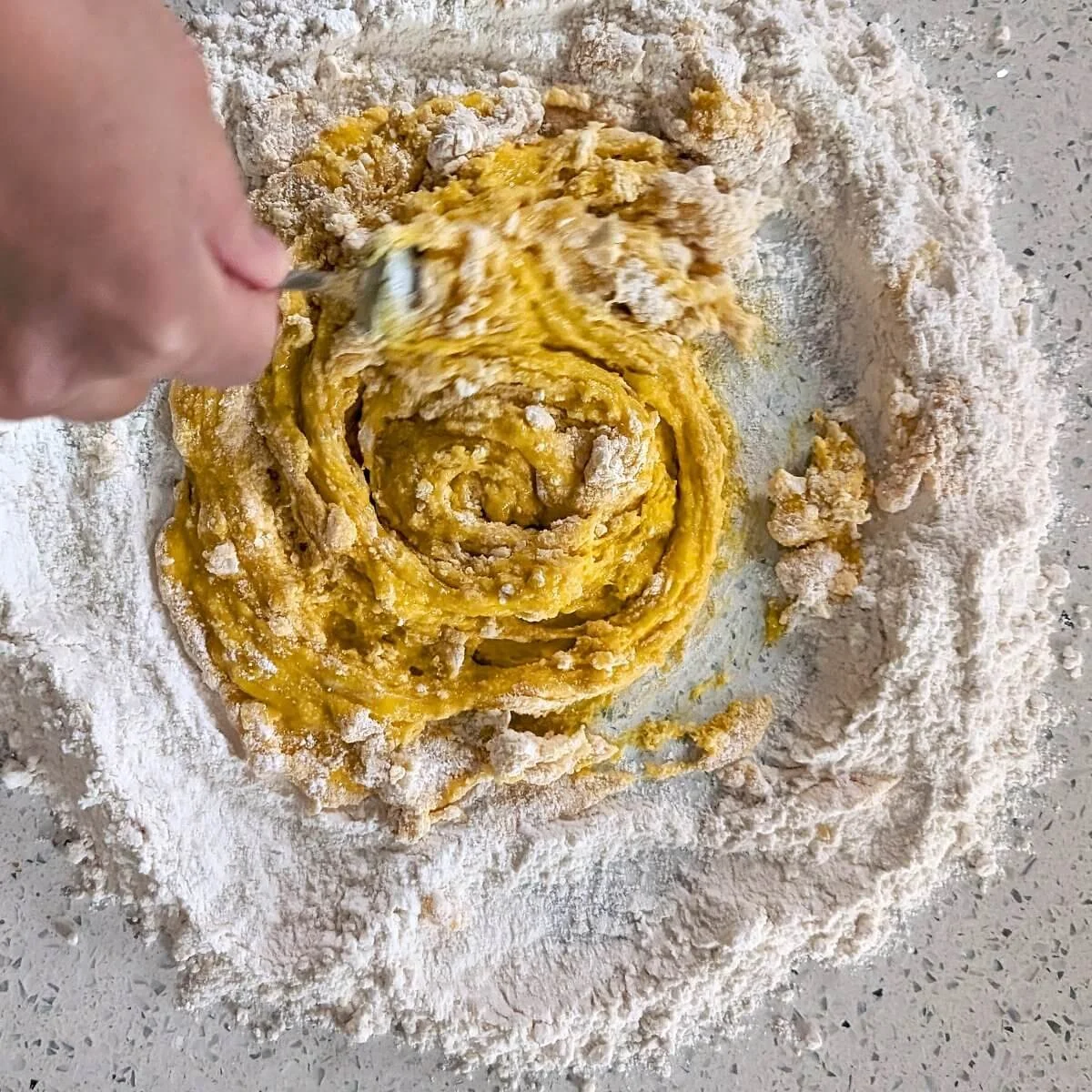 Fork gradually pulling flour into the beaten eggs to begin forming pasta dough