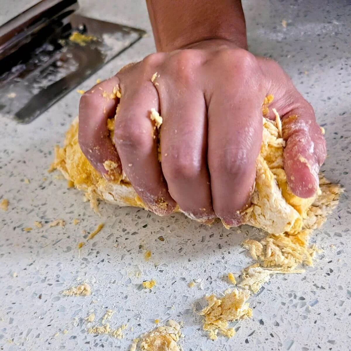 Firmly squeezing and compressing the pasta dough to help it form a cohesive mass