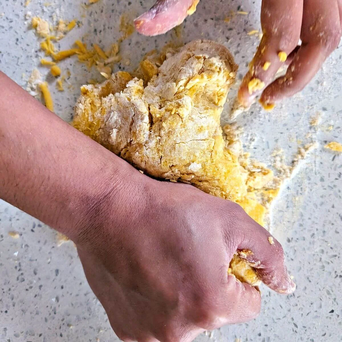 Hands pressing crumbly pasta dough together on the countertop before kneading