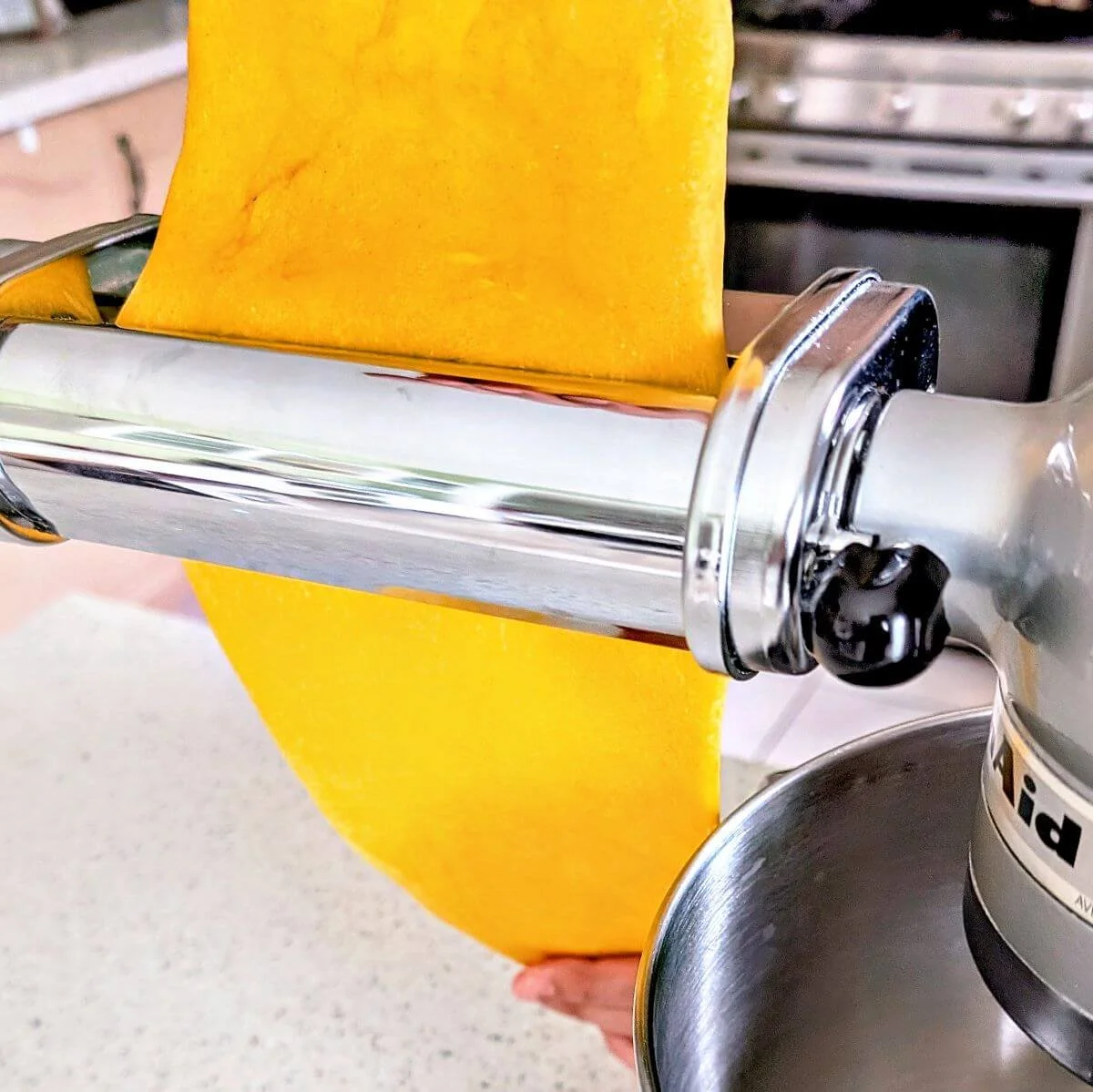 Fresh pasta dough sheet being fed through a pasta machine on the widest setting
