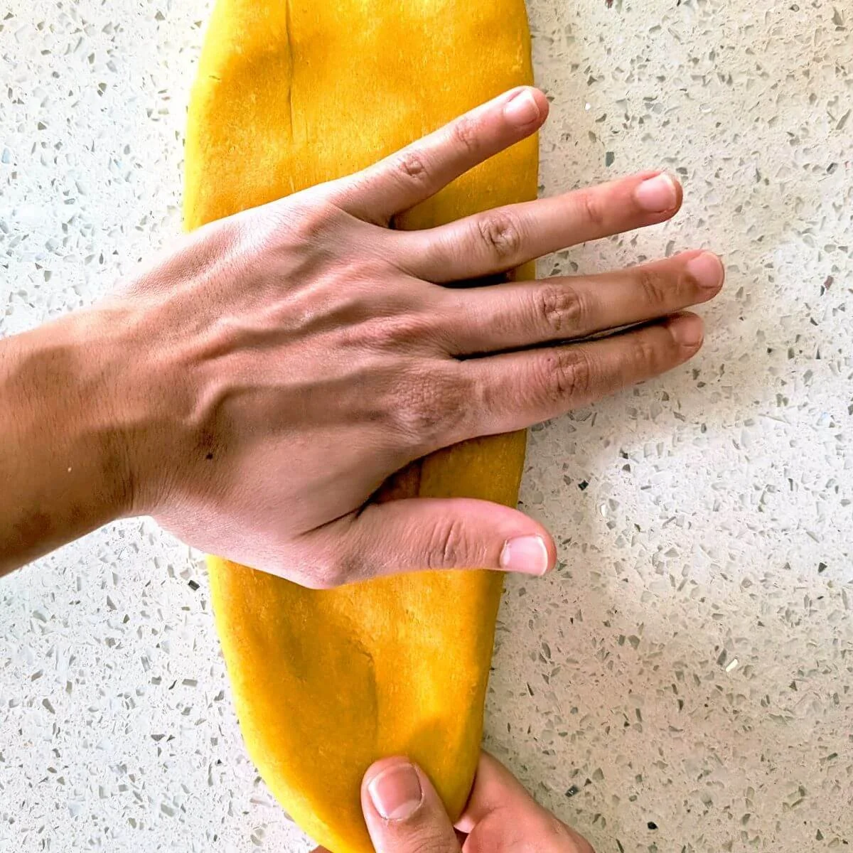 Hand pressing fresh pasta dough into a flat oval on a countertop before rolling