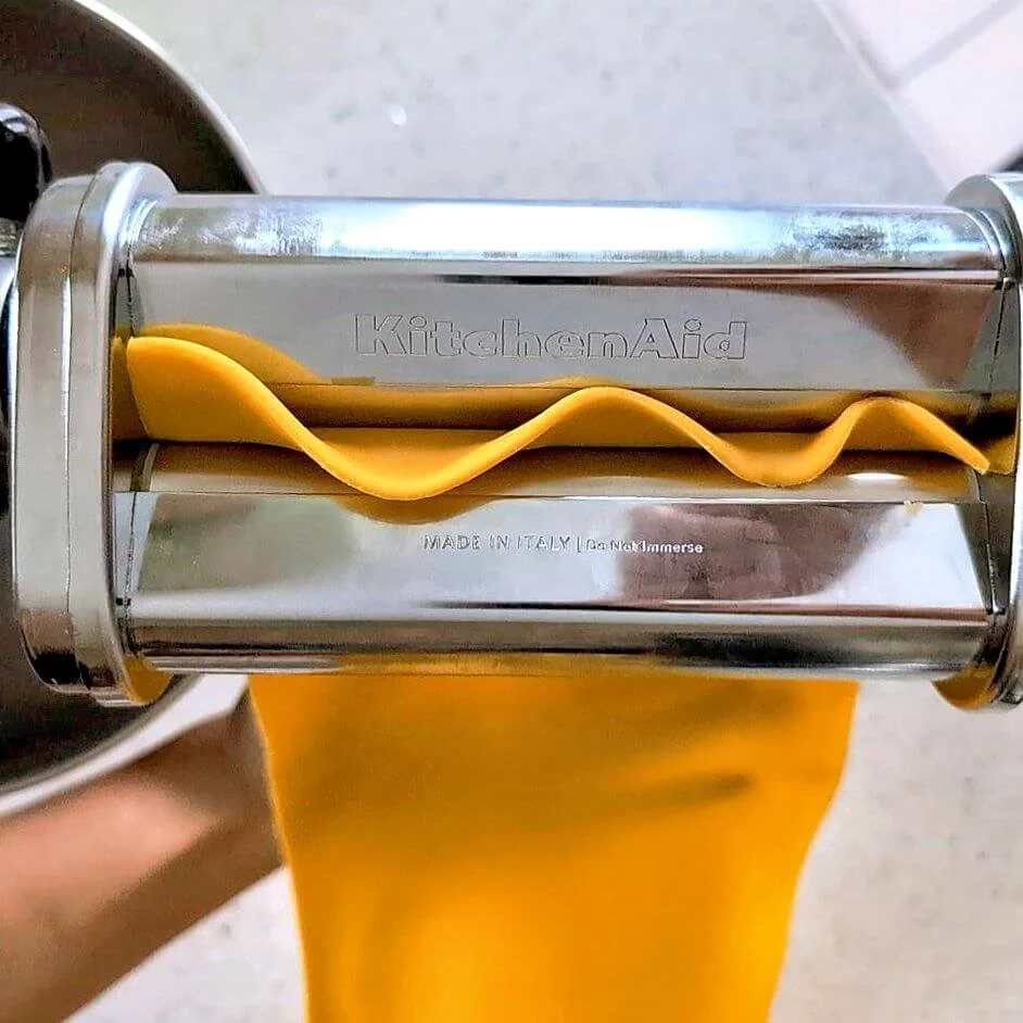 Overhead of fresh pasta sheet passing through a pasta machine with a palm catching it as it comes out of the machine