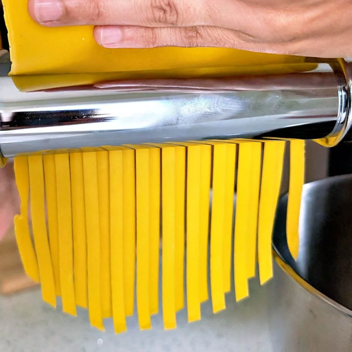 Fresh pasta being cut into fettuccine through a pasta machine attachment
