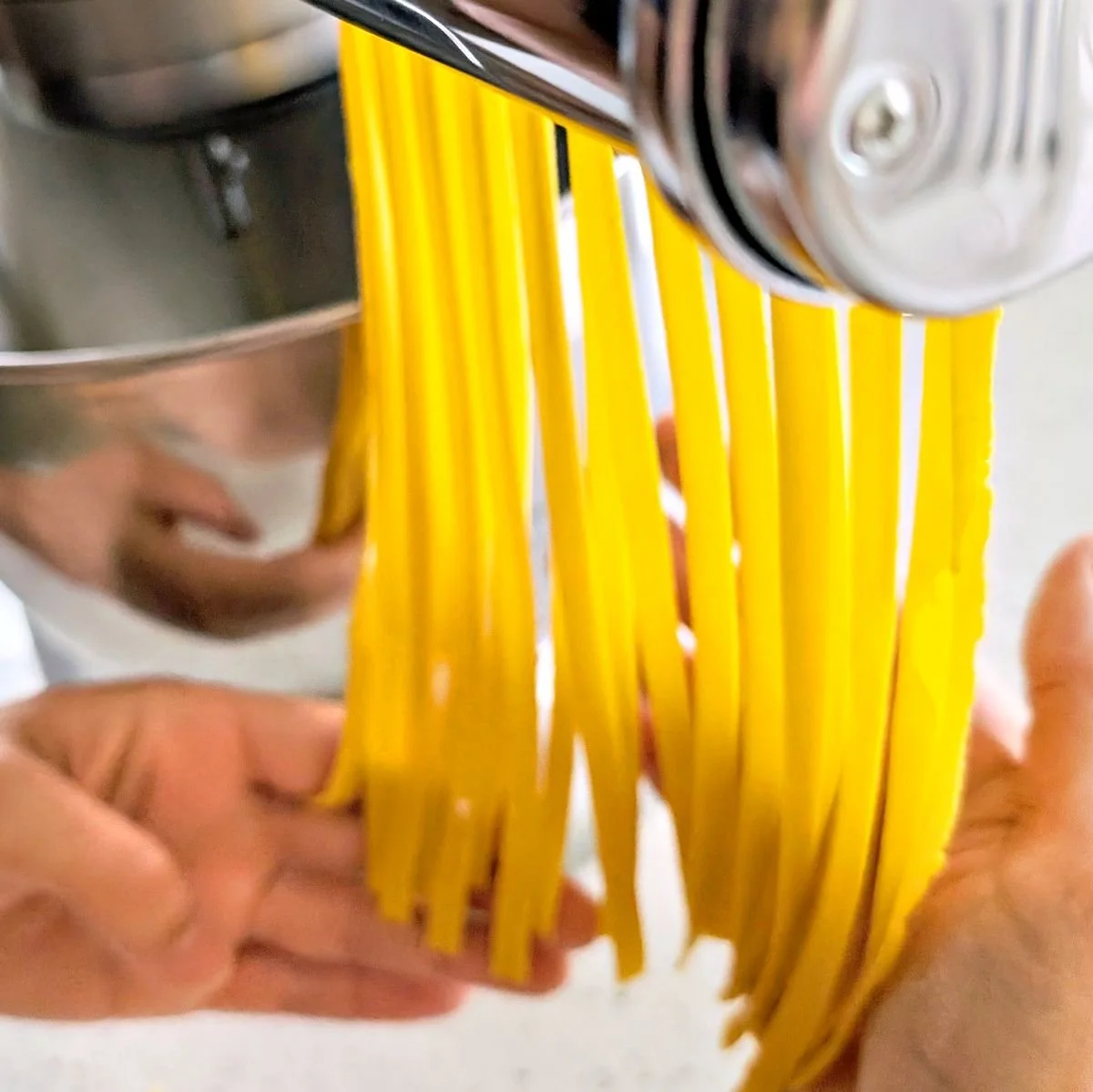 Hands catching freshly cut pasta strands as they come out of the pasta machine