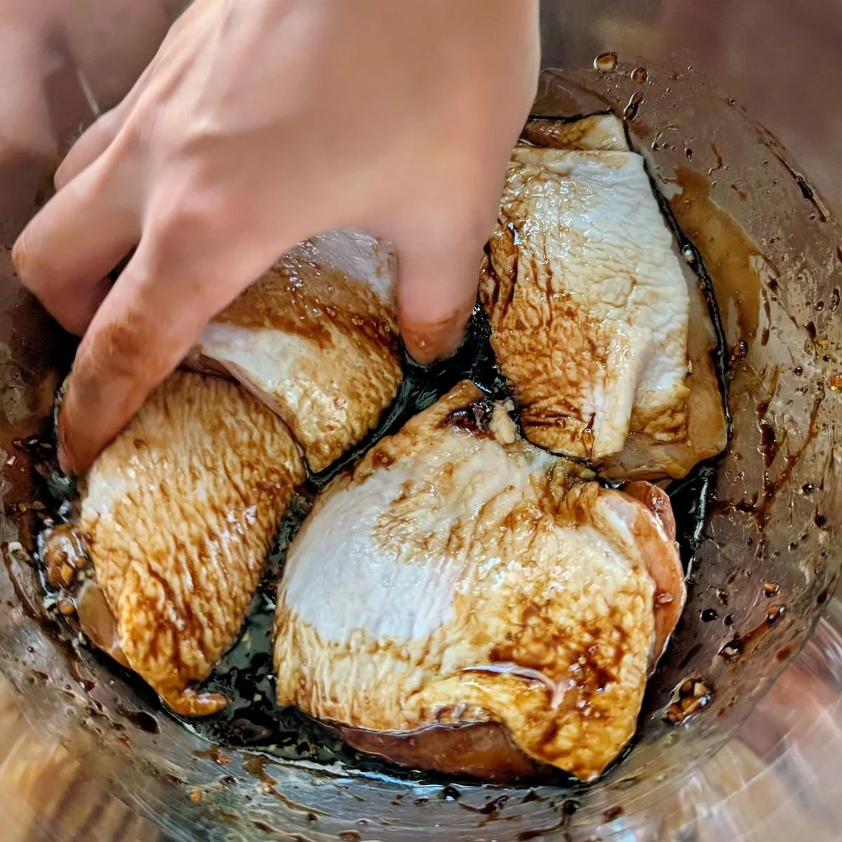 Bone-in chicken thighs being tossed in soy balsamic marinade in a bowl