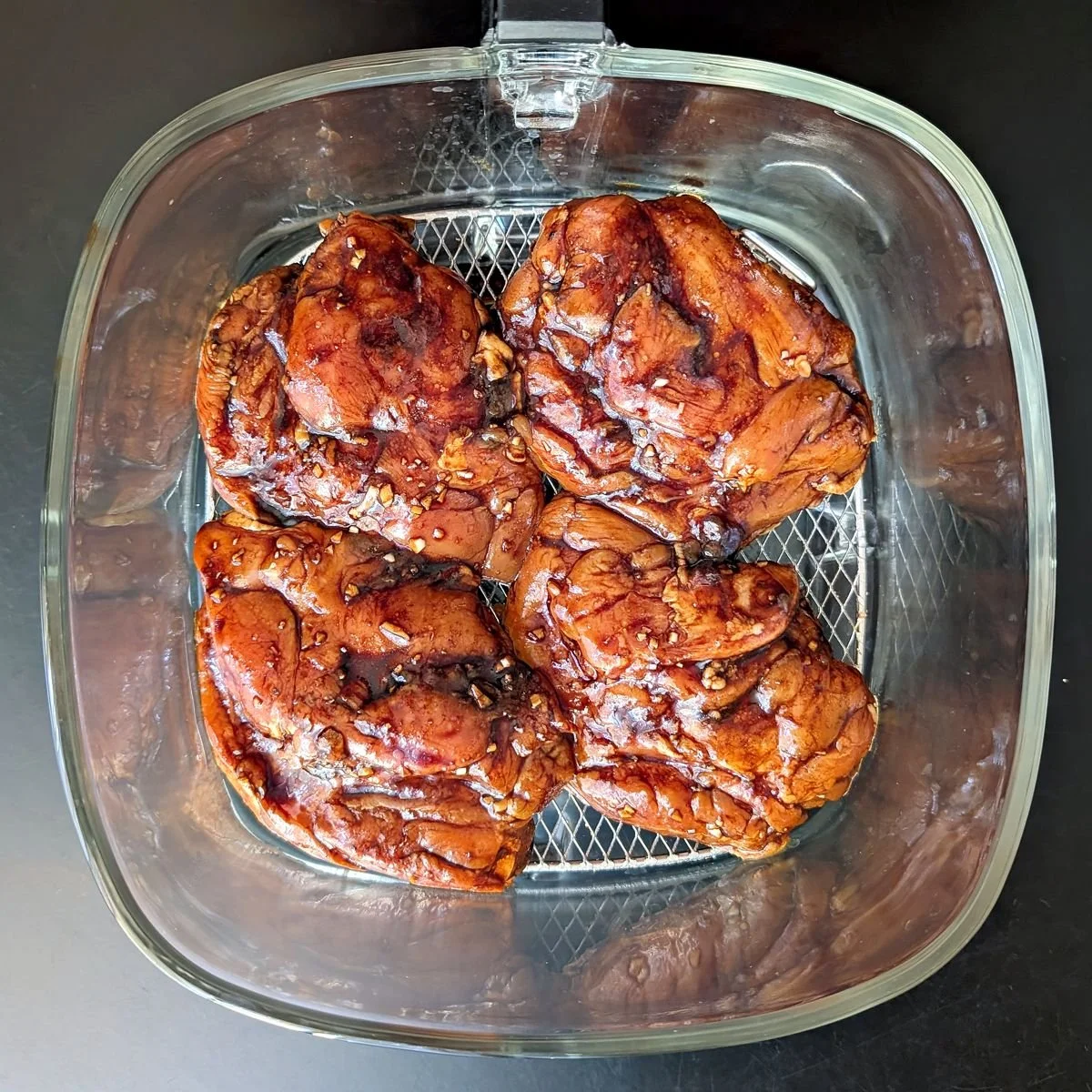 Balsamic marinated chicken thighs arranged in a single layer in an air fryer basket