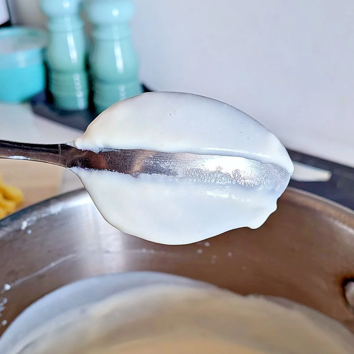 Nappe test showing a smooth white sauce coating a spoon before adding the cheese