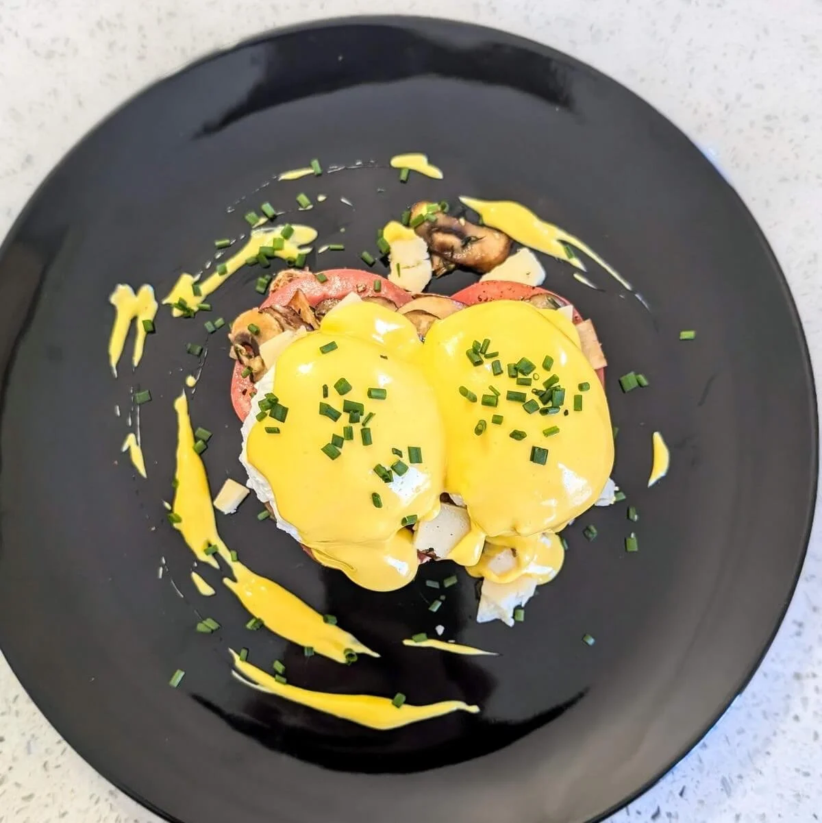 Homemade stick blender hollandaise on eggs benedict on a black plate