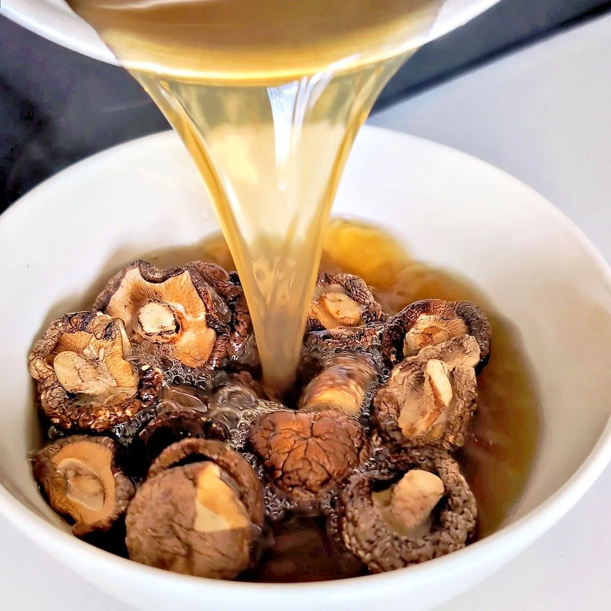Hot vegetable broth being poured over dried shiitake mushrooms