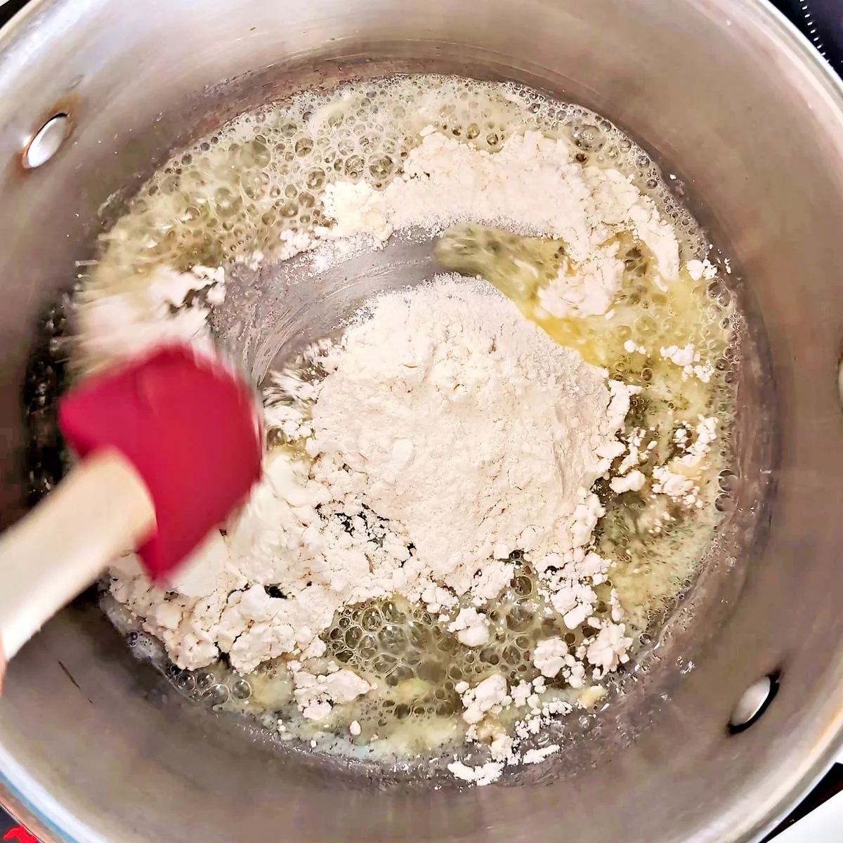 Adding flour to melted butter to begin making a roux
