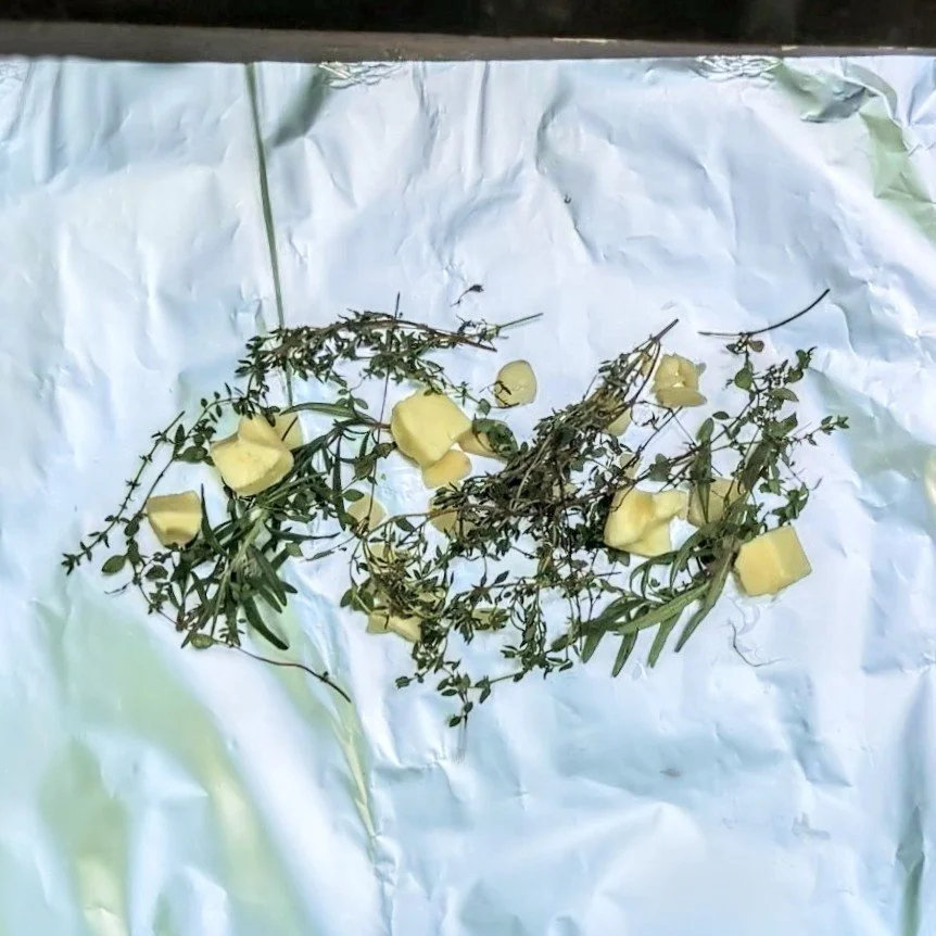 Garlic, rosemary, thyme, and butter layered on foil for resting woodfire grilled flank steak at a campsite