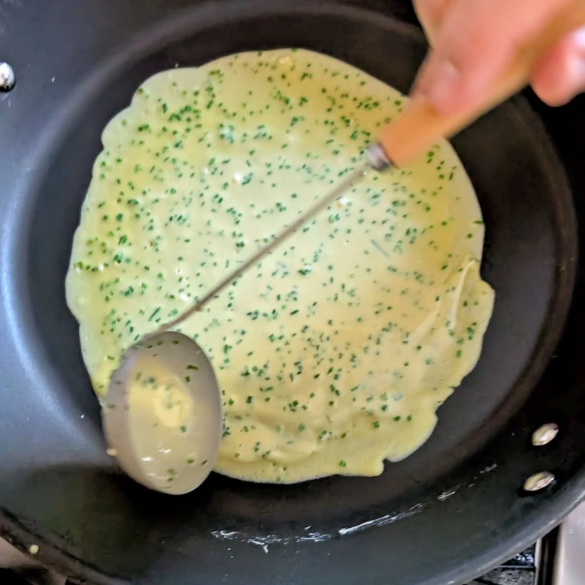 Spreading chive crêpe batter into a thin layer in a nonstick skillet