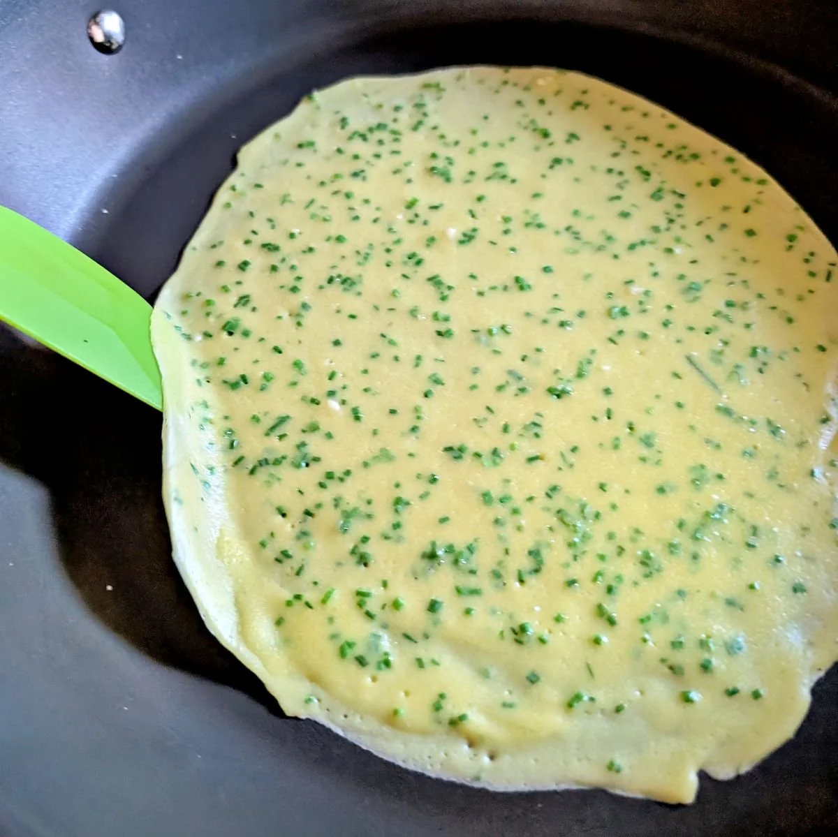 Chive crêpe edges being lifted before flipping