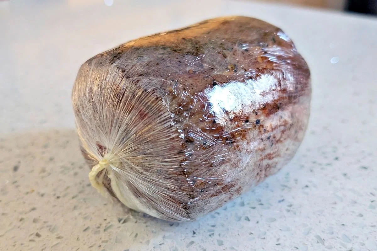 Beef tenderloin shaped into a tight cylinder in plastic wrap for beef Wellington