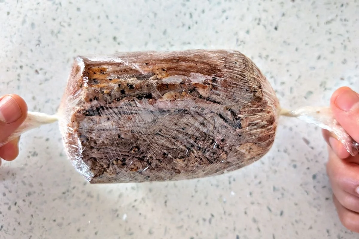 Twisting plastic wrap tightly around the seared beef tenderloin to shape it