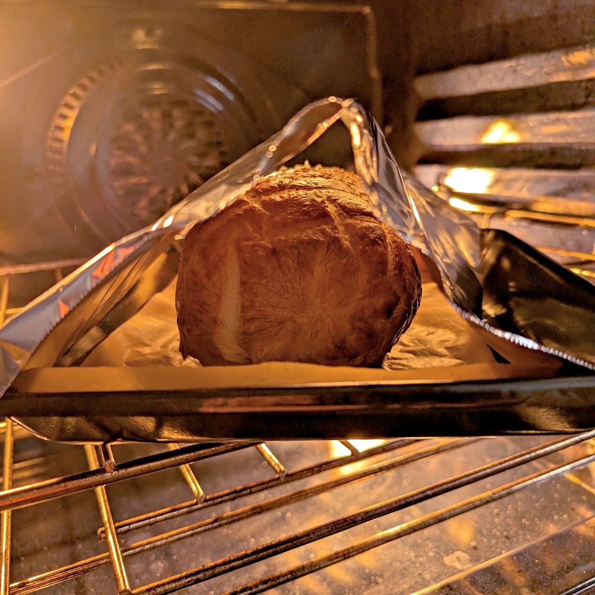 Beef Wellington baking under a loose aluminum foil tent with space above the puff pastry