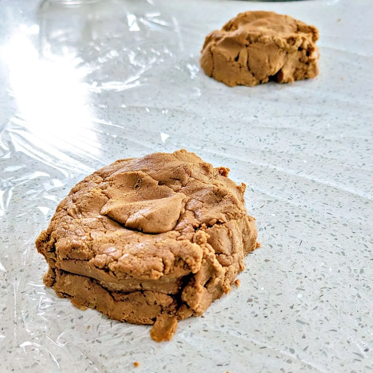 Gingerbread dough pressed into two portions on plastic wrap