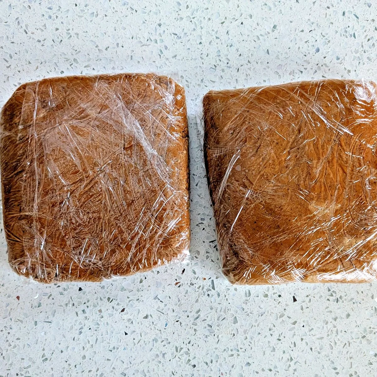 Two portions of gingerbread dough wrapped in plastic for chilling