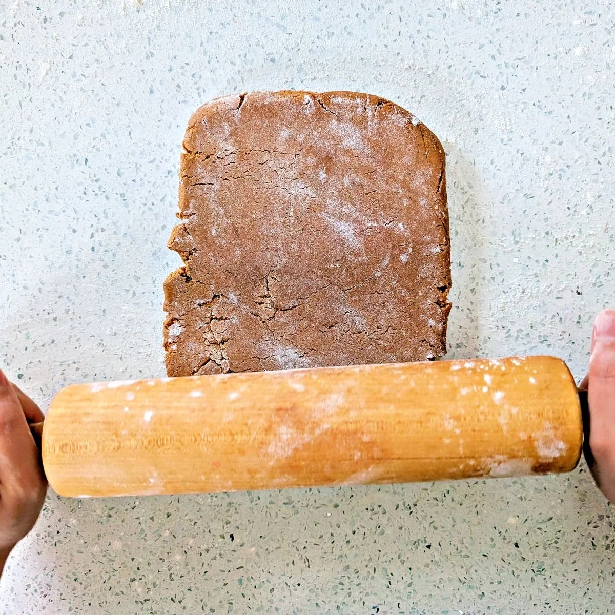 Chilled gingerbread dough being rolled out with a rolling pin on a floured counter