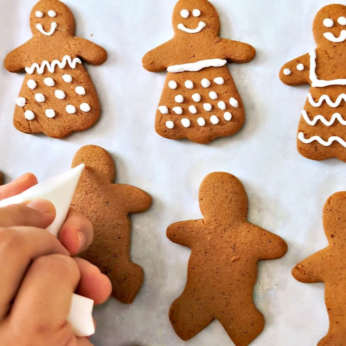 Hand piping white royal icing onto gingerbread people cookies